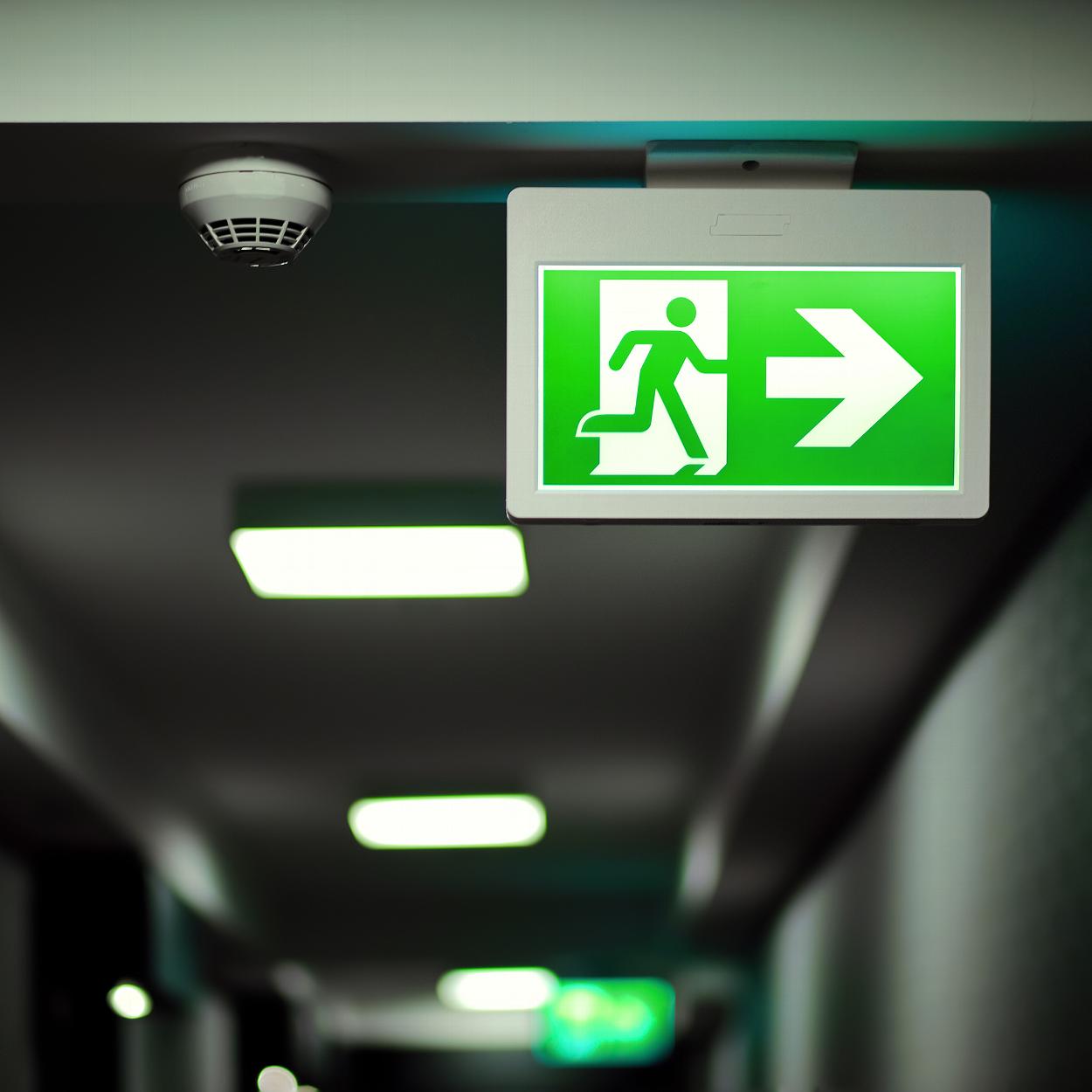 Green emergency exit sign with fire alarm on ceiling